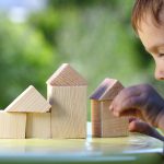 boy raises his hand to the house from wooden cubes